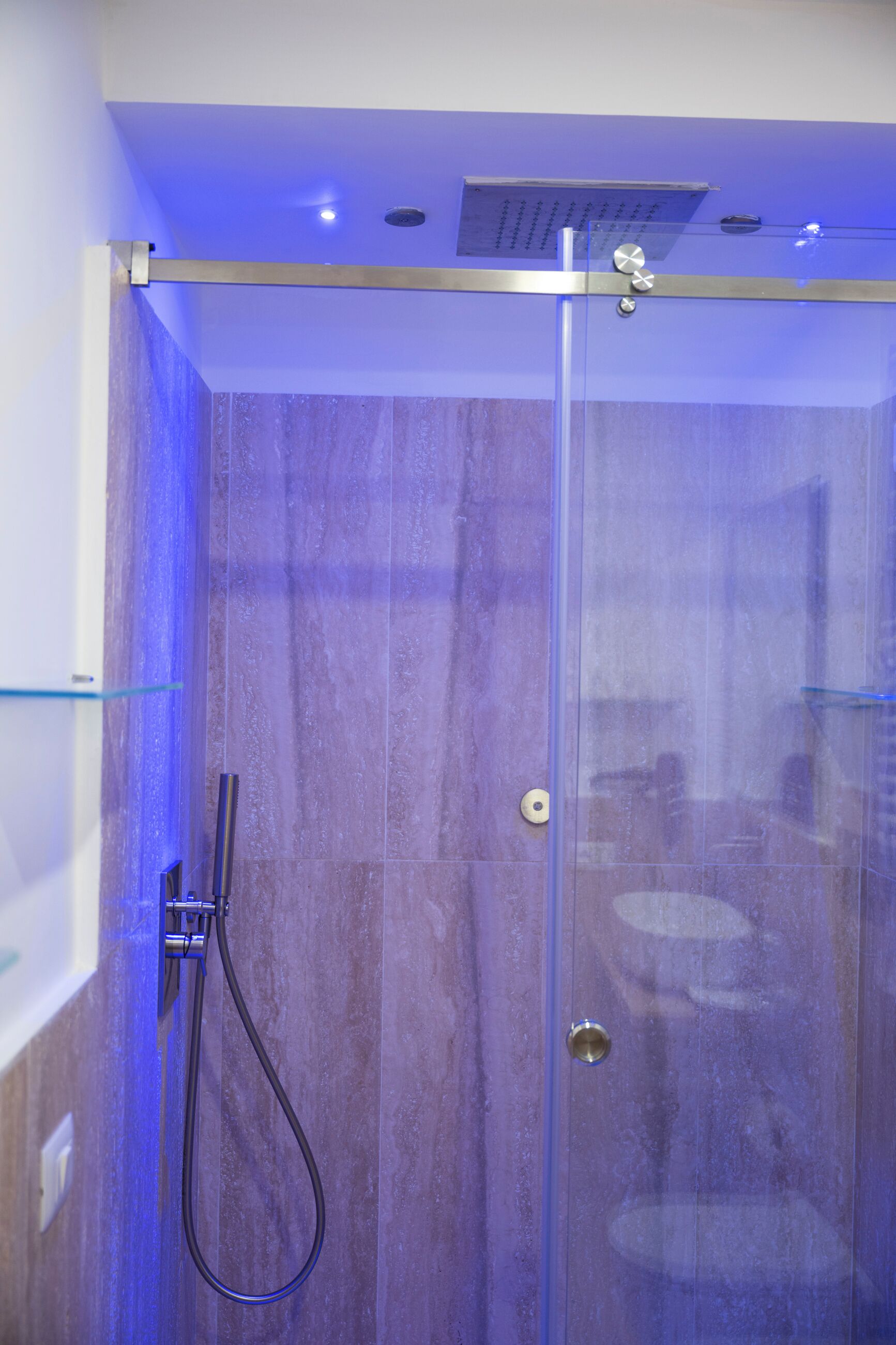 Ducha envuelta en vidrio, con cabezal de ducha manual, panel de control y sistema de ventilación.