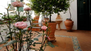 A courtyard with potted plants and a tree, a tiled floor, and a building with a door and windows. - Hotel Antica Repubblica (Amalfi)