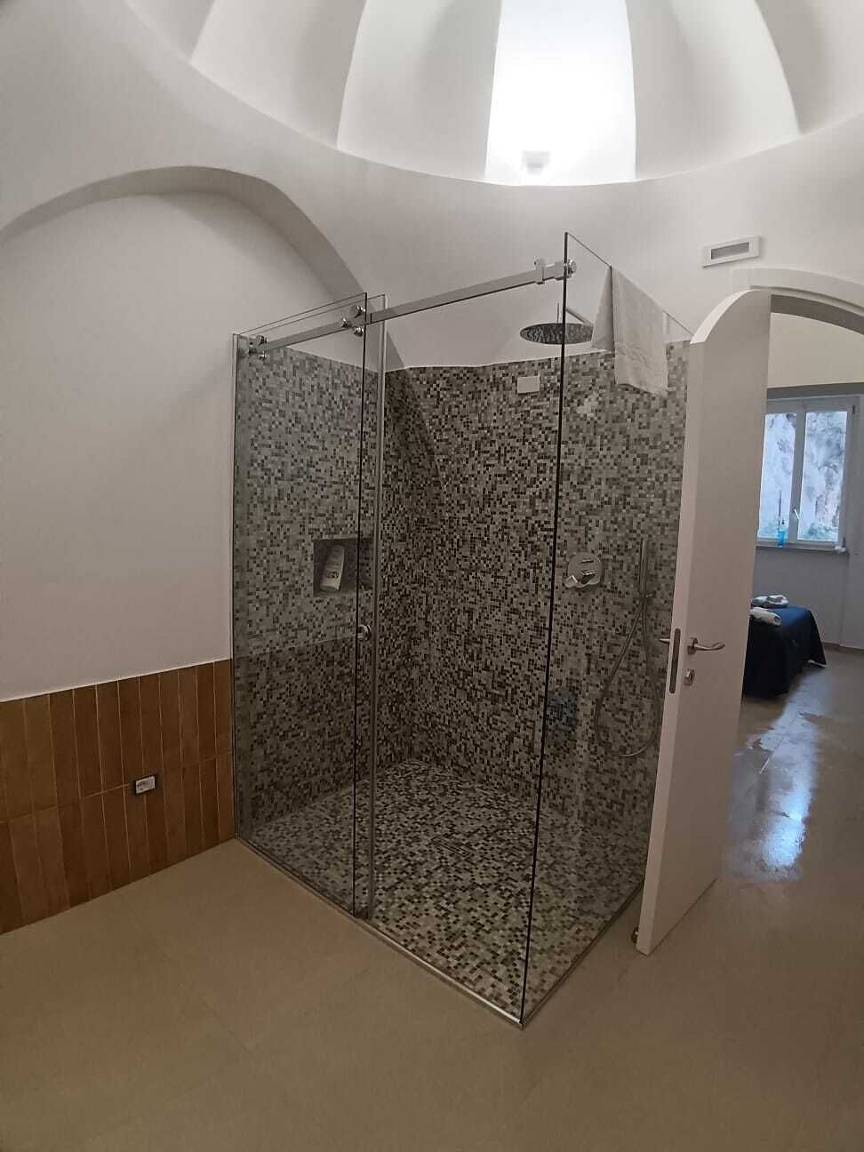 Habitación con ducha de vidrio, piso de baldosas y techo alto con tragaluz.