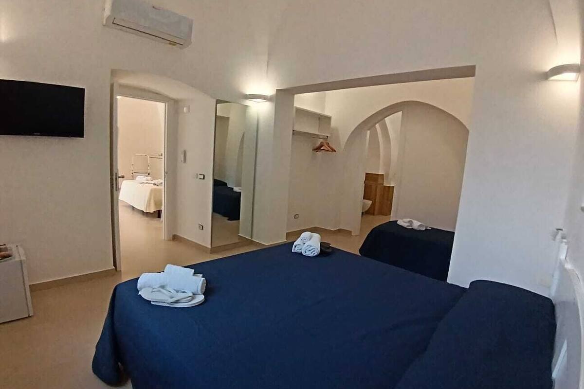 A hotel room with a bed, a TV, an air conditioner, and a mirror.