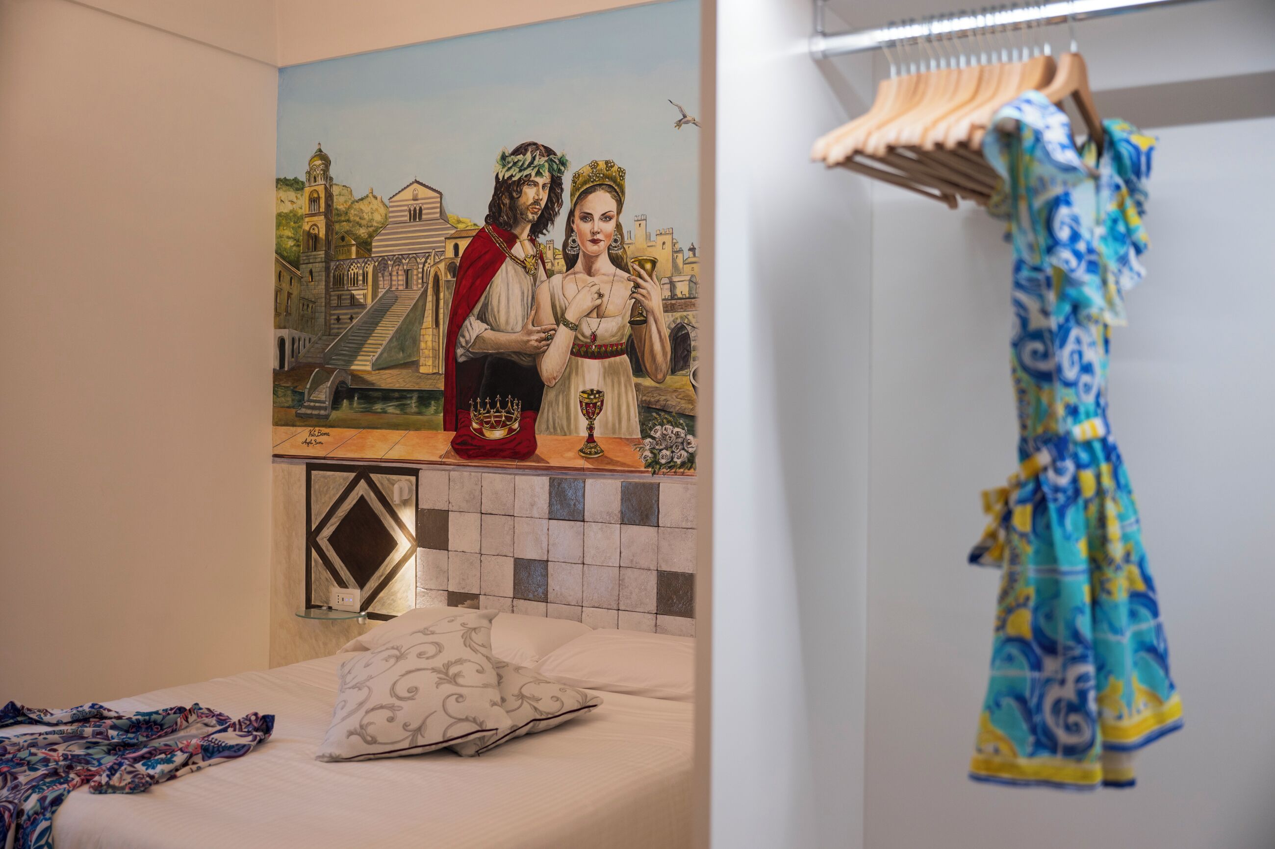 Un dormitorio con un mural de una pareja, una cama con un cojín estampado y un perchero.