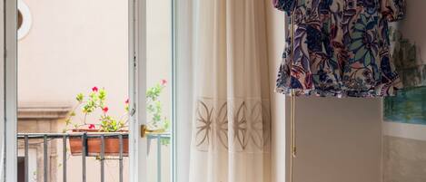 A room with a balcony, a white desk, a chair, and a hanging garment.