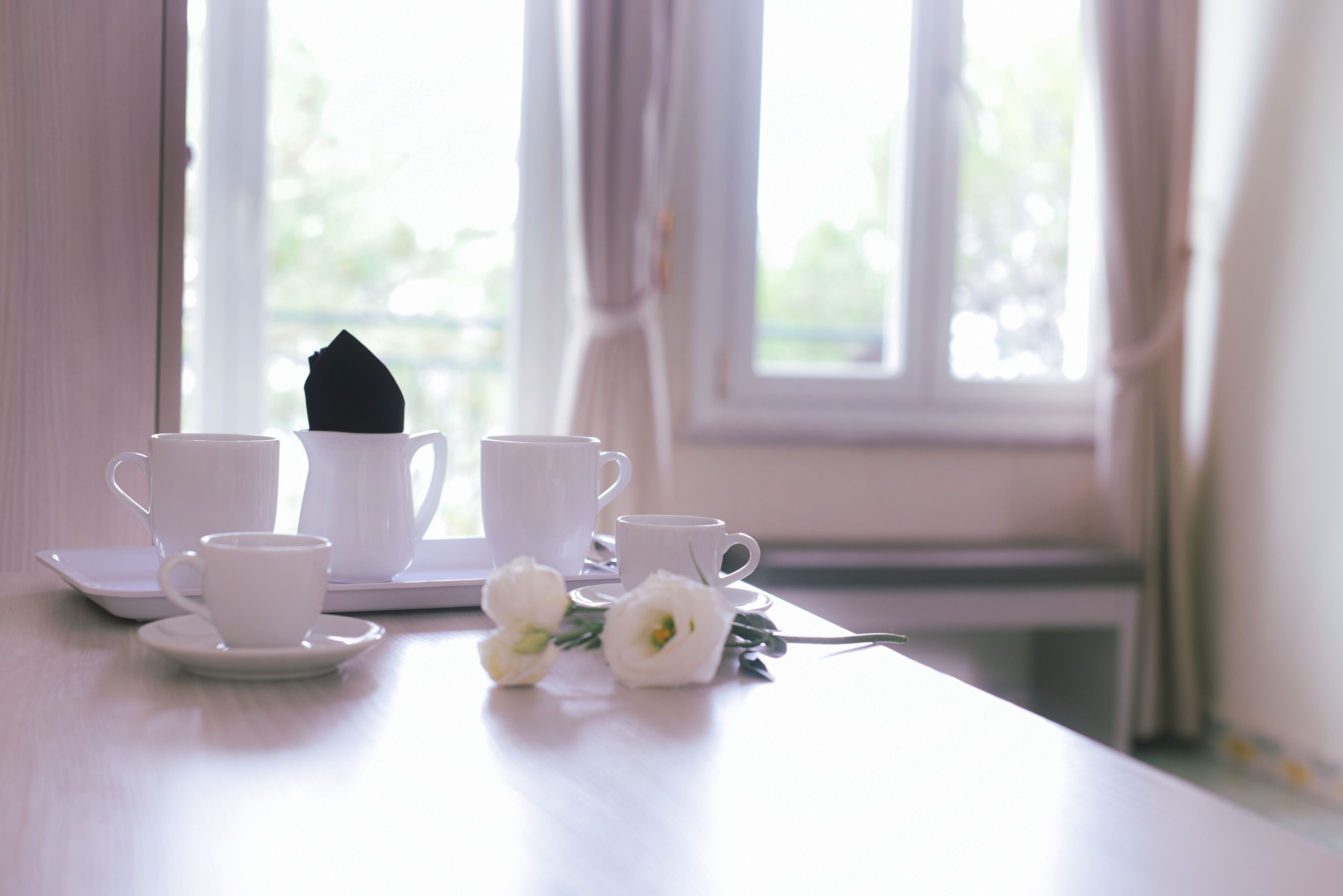 Une table avec des tasses et des soucoupes blanches, une serviette noire et des fleurs blanches.