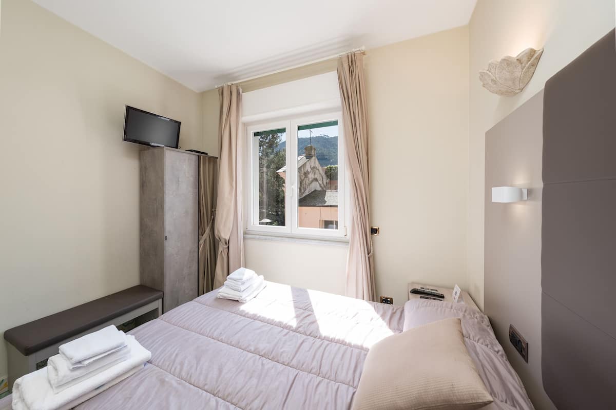 A bedroom with a bed, a TV on a cabinet, and a window with curtains.