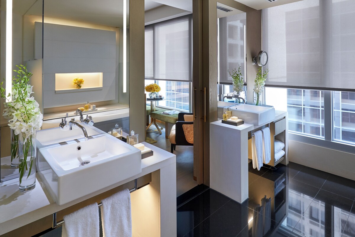 Une salle de bain moderne avec deux lavabos, un grand miroir et une fenêtre qui laisse entrer la lumière naturelle.