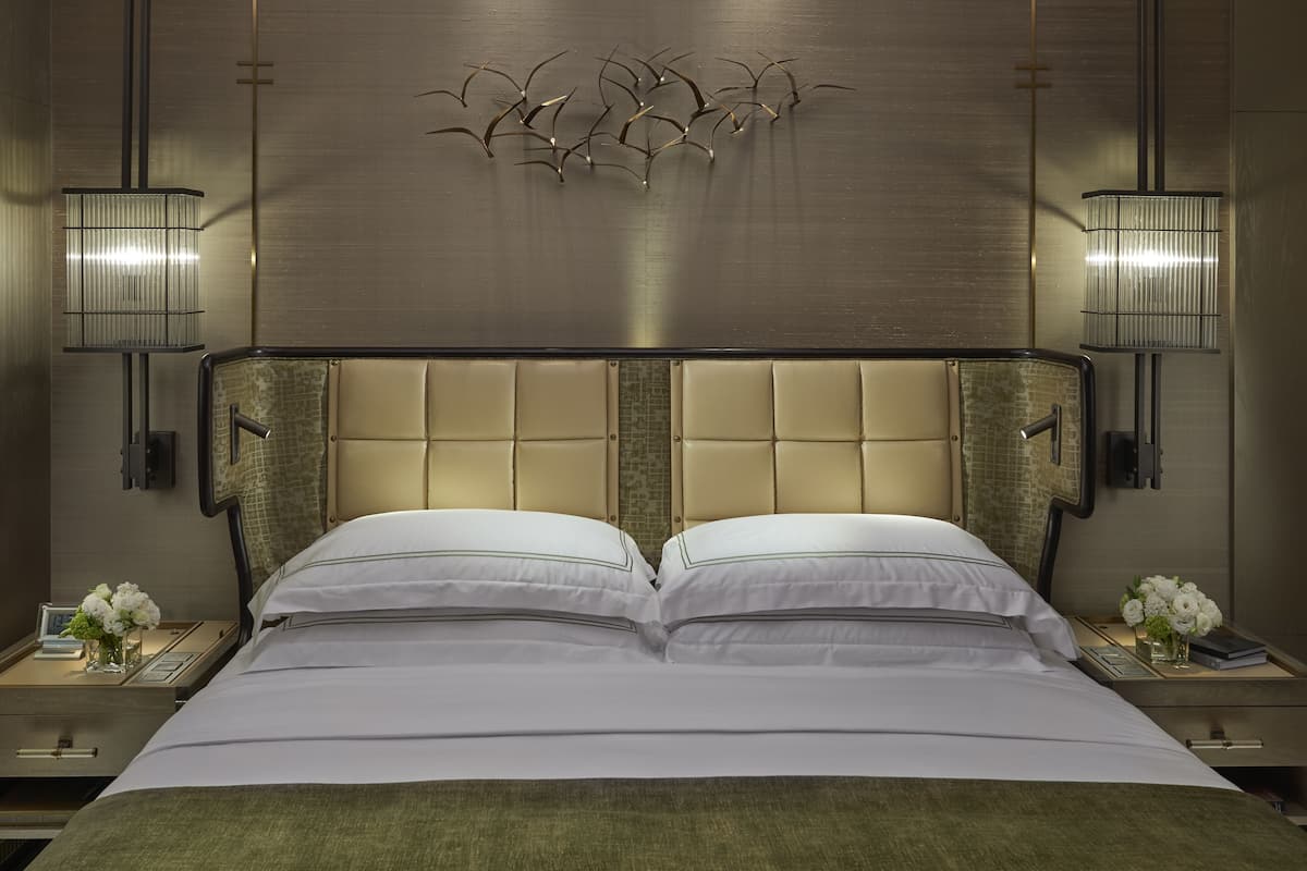Een hotelkamer met een groot bed, twee nachtkastjes, een wandlamp en een decoratieve wandversiering.