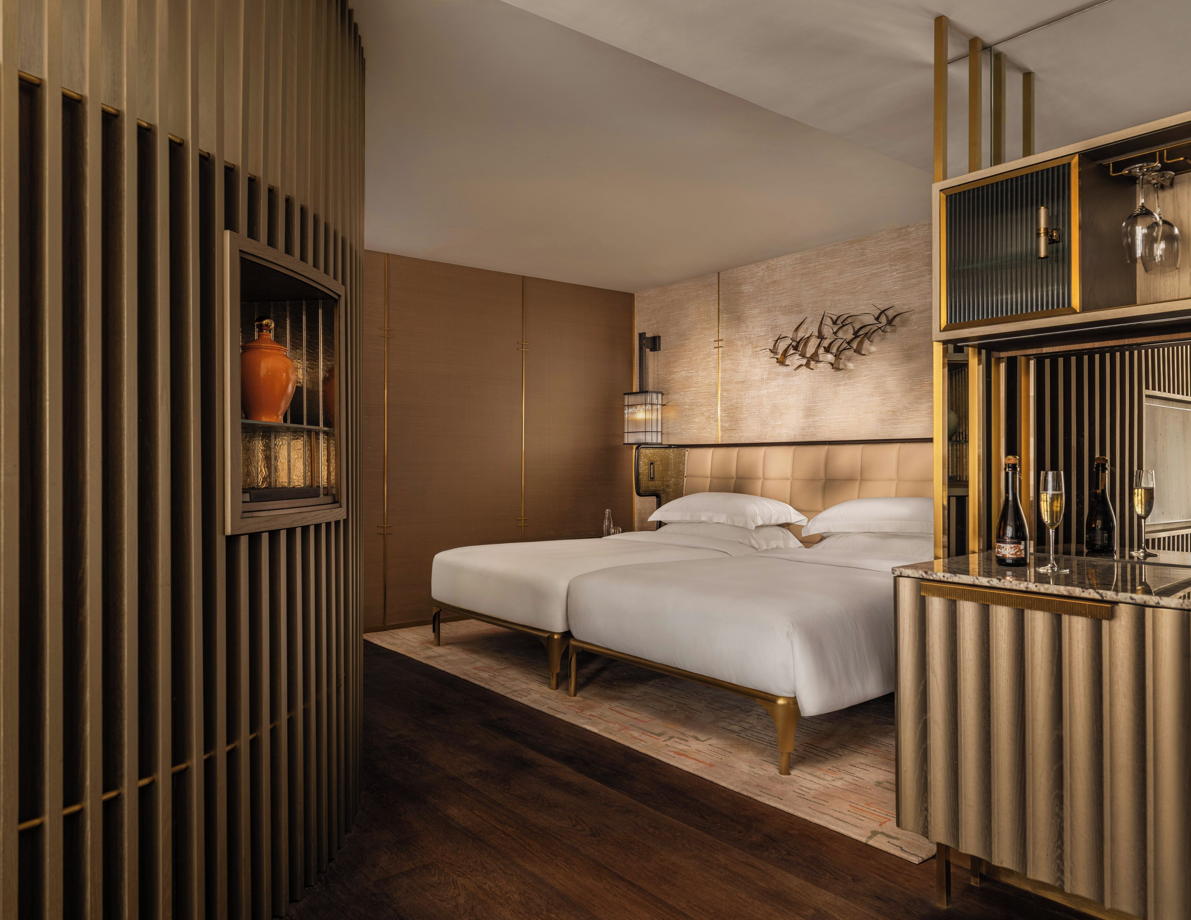 A hotel room with a bed, bedside tables, a wall-mounted shelf with a vase, and a decorative wall piece.