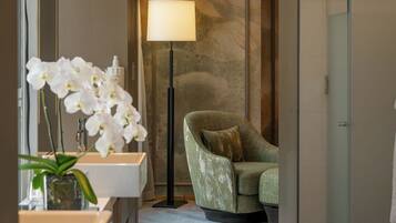 A modern bathroom with a marble floor, a green armchair, a floor lamp, and white orchids.