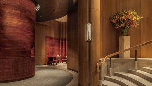 Eine Lobby mit einer gewölbten roten Wand, einem hölzernen Empfangsschalter, einer Treppe und einer Blumenvase.