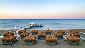 Un resort en la playa con cabañas de techo de paja y un muelle que lleva a una cabaña sobre el agua.