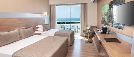 A hotel room with two beds, a desk, a chair, a TV, and a balcony with a view of the sea.