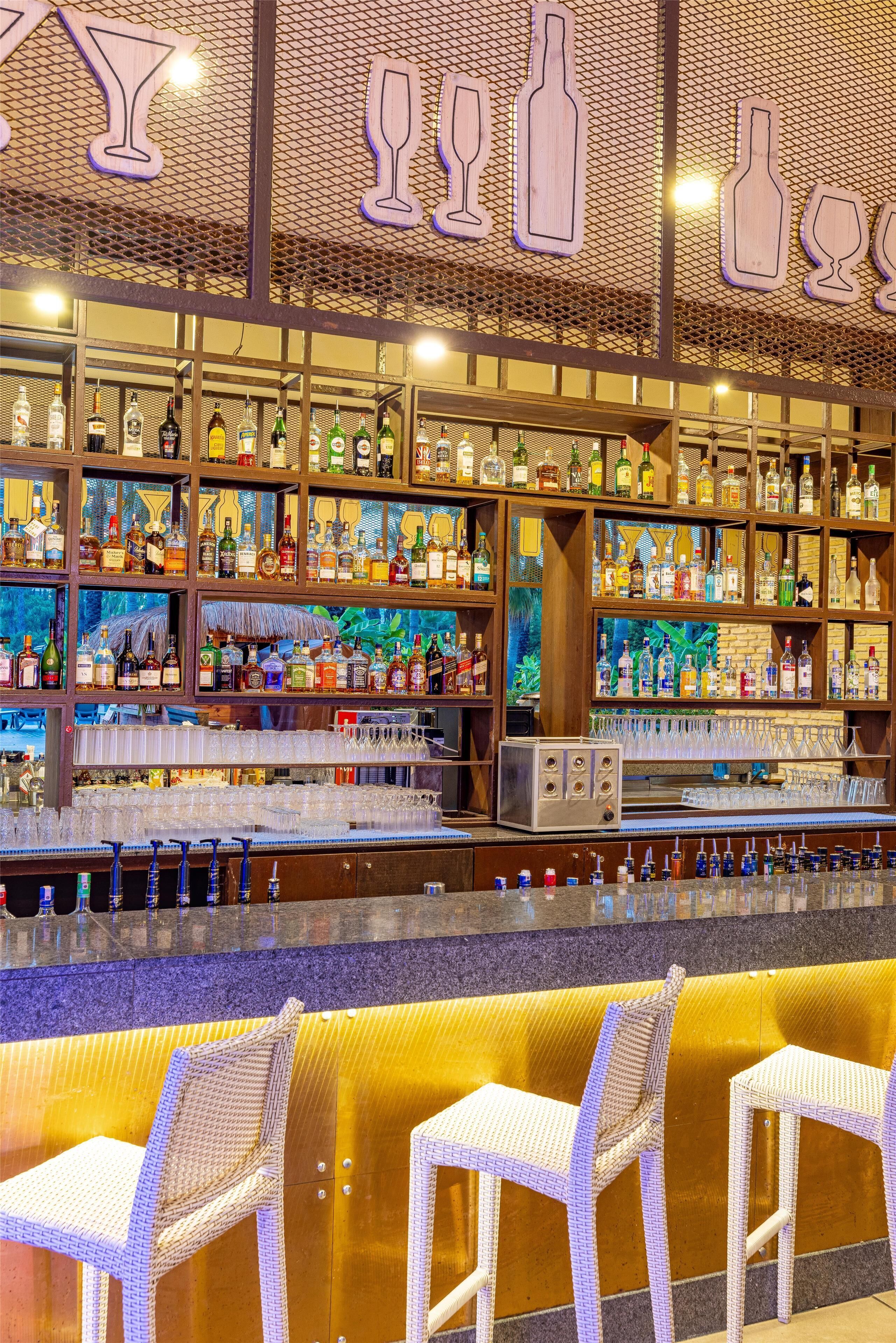 A bar area with shelves of liquor bottles, a bar counter, and wicker chairs.