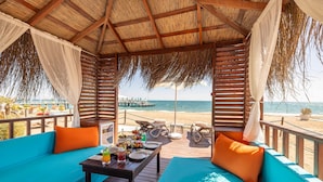 A beachside cabana with a wooden deck, seating area, and a table set with drinks and snacks. - Concorde De Luxe Resort Lara Antalya - Prive Ultra All Inclusive (Antalya)