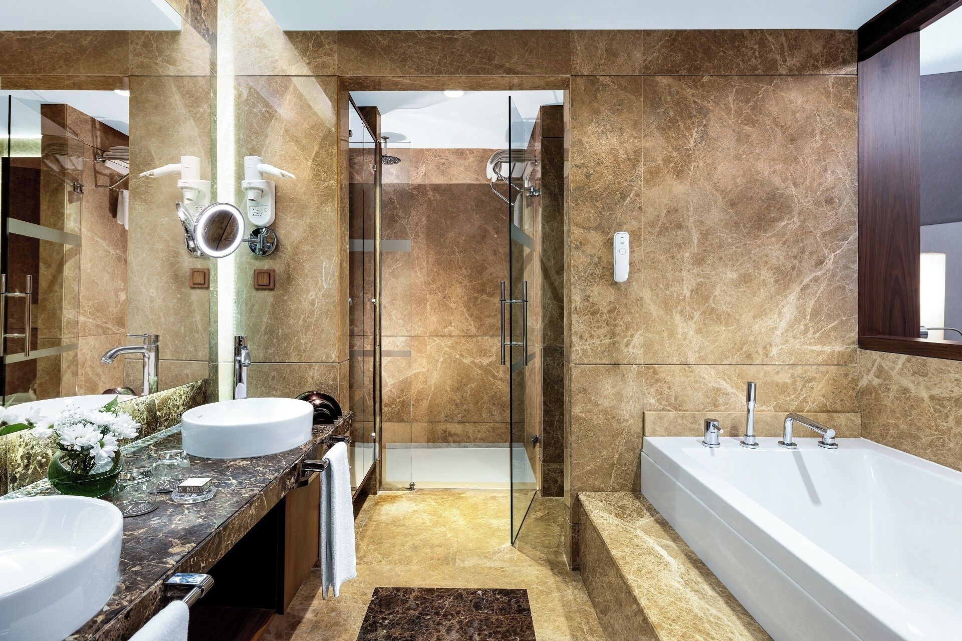 A modern bathroom with a large bathtub, two sinks, a glass shower enclosure, and marble flooring.