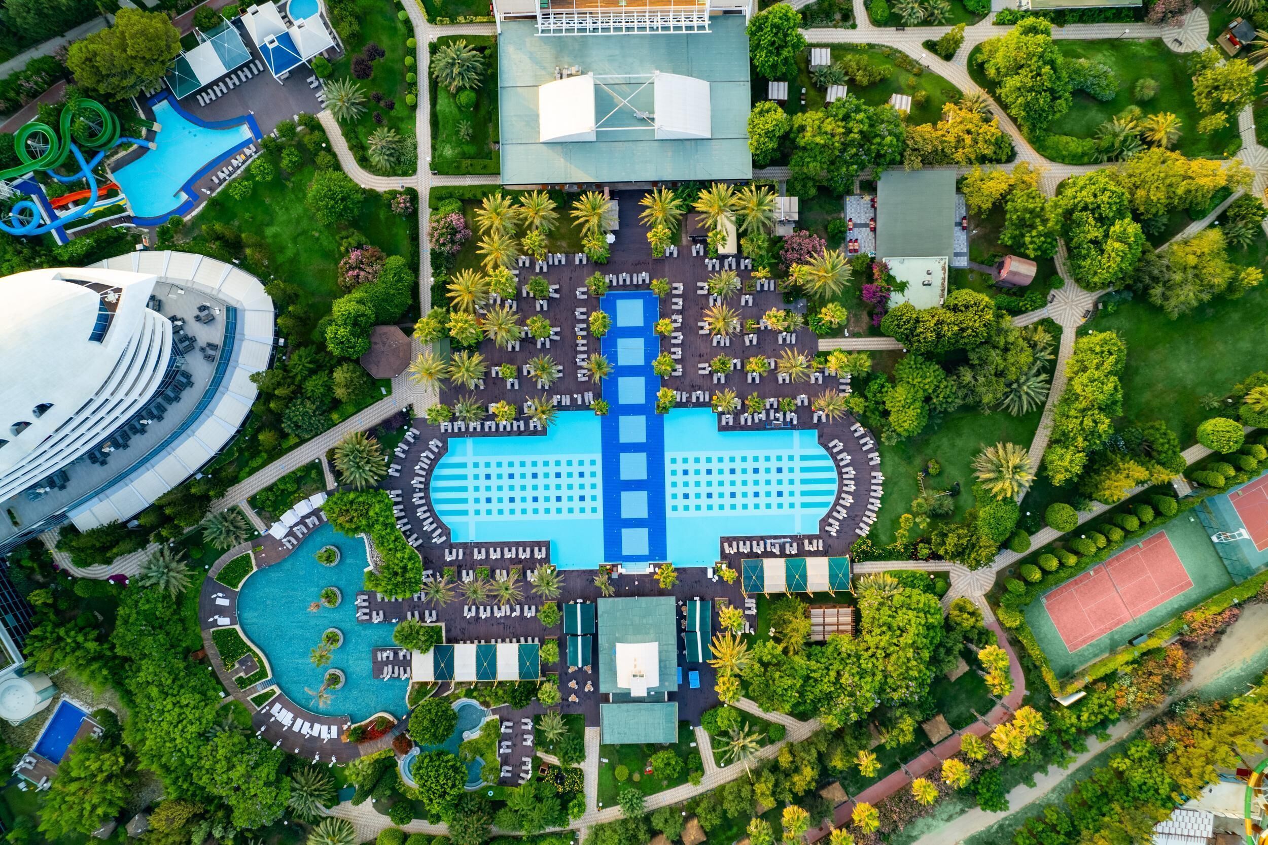 An aerial view of a resort with a large central pool, multiple smaller pools, and a tennis court.