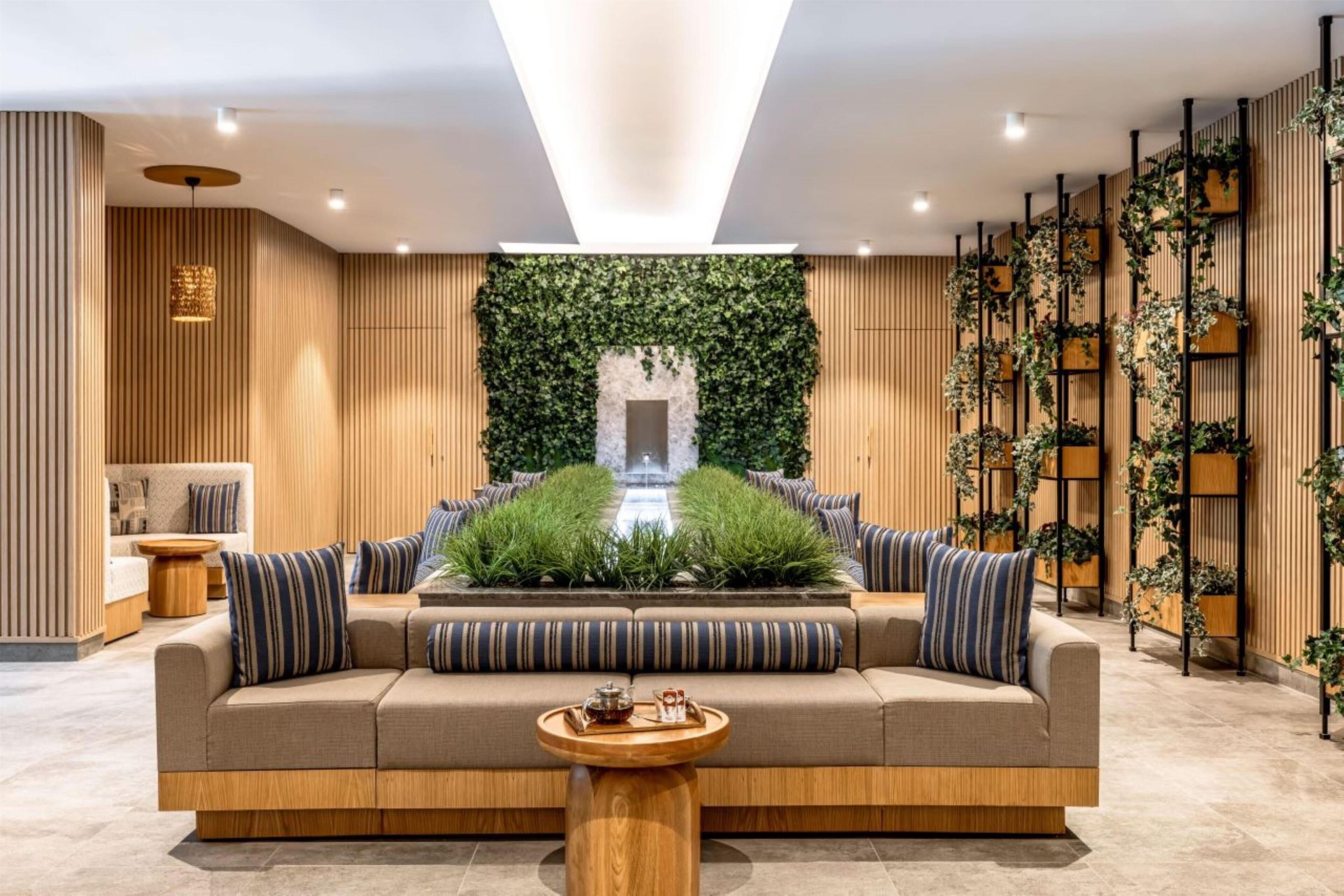 Un vestíbulo moderno con un sofá, una mesita y una pared revestida de paneles de madera y vegetación.