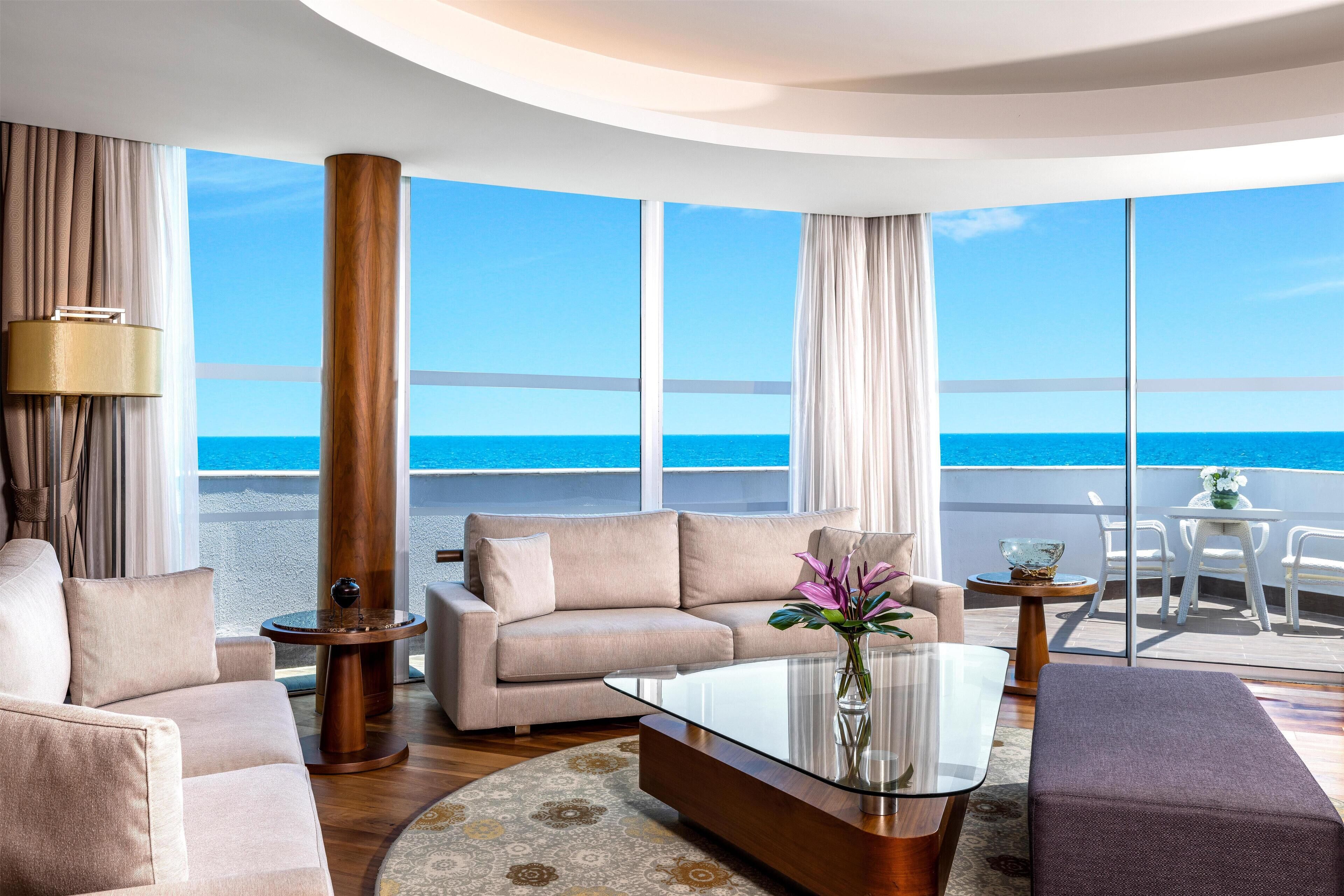 Una sala de estar moderna con un ventanal grande con vista al mar, un sofá, una mesita de centro y una mesita auxiliar.