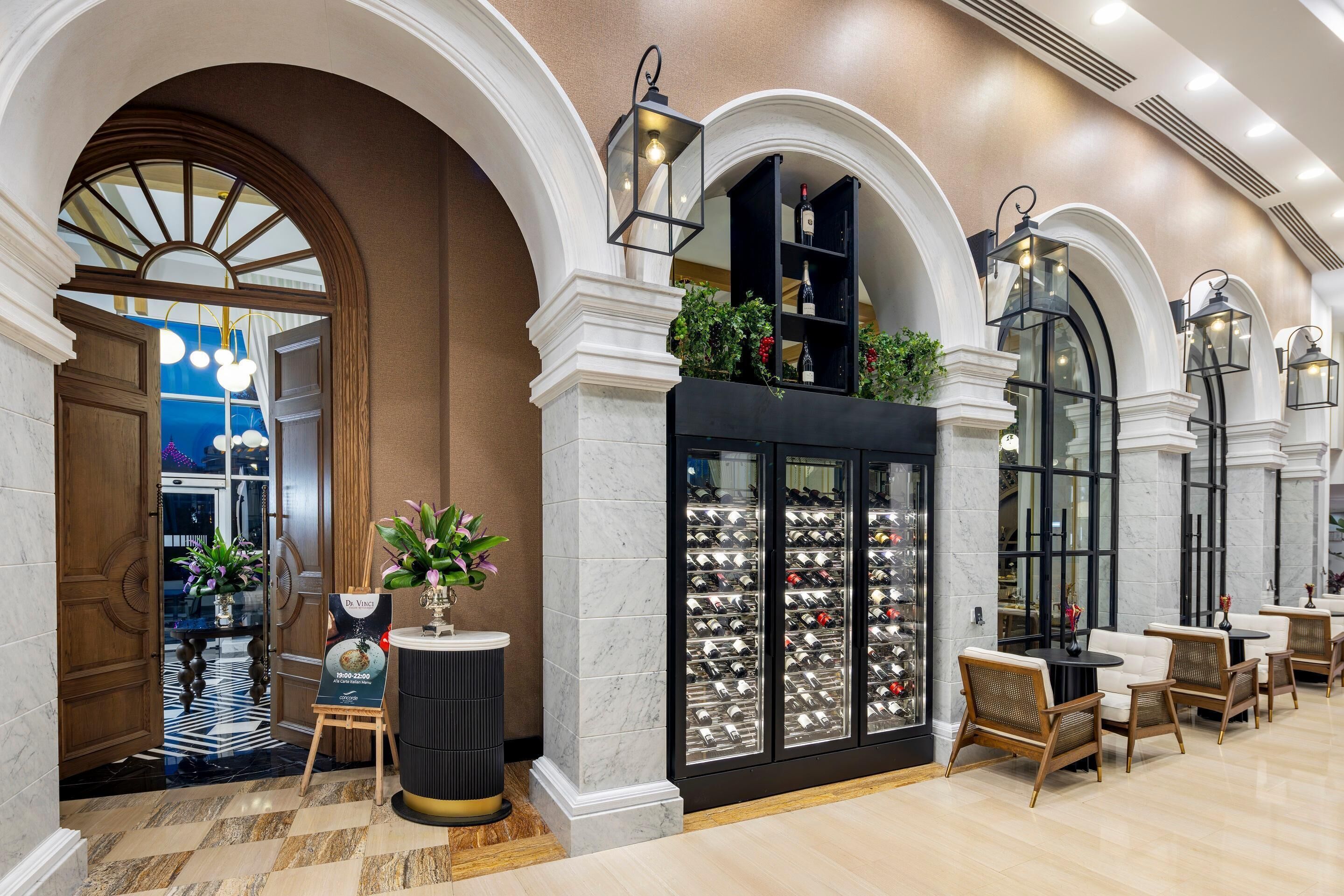 A lobby with marble flooring, wooden columns, and a wine display.