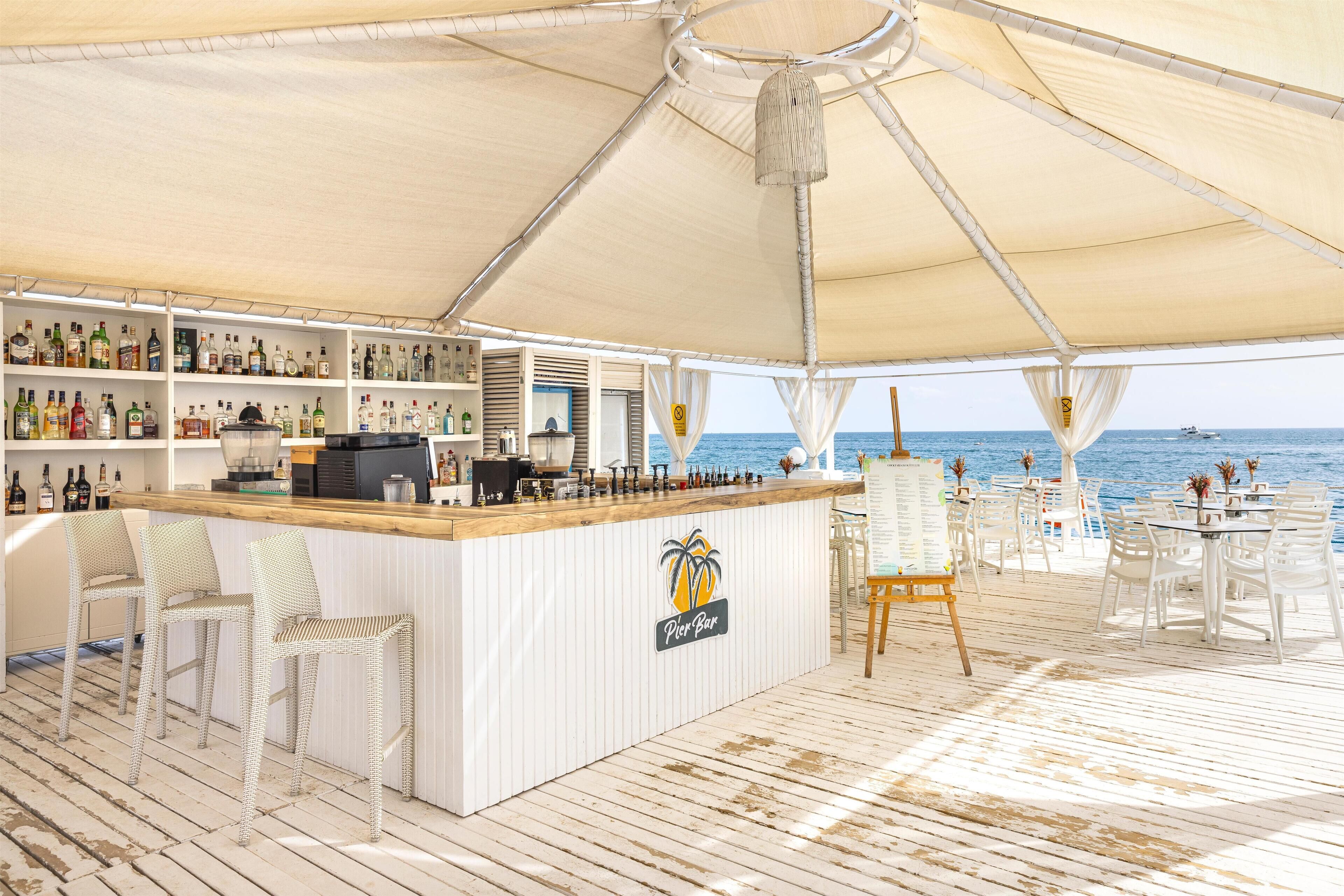 A Pier Bar with a wooden counter, white wicker chairs, and a view of the sea.