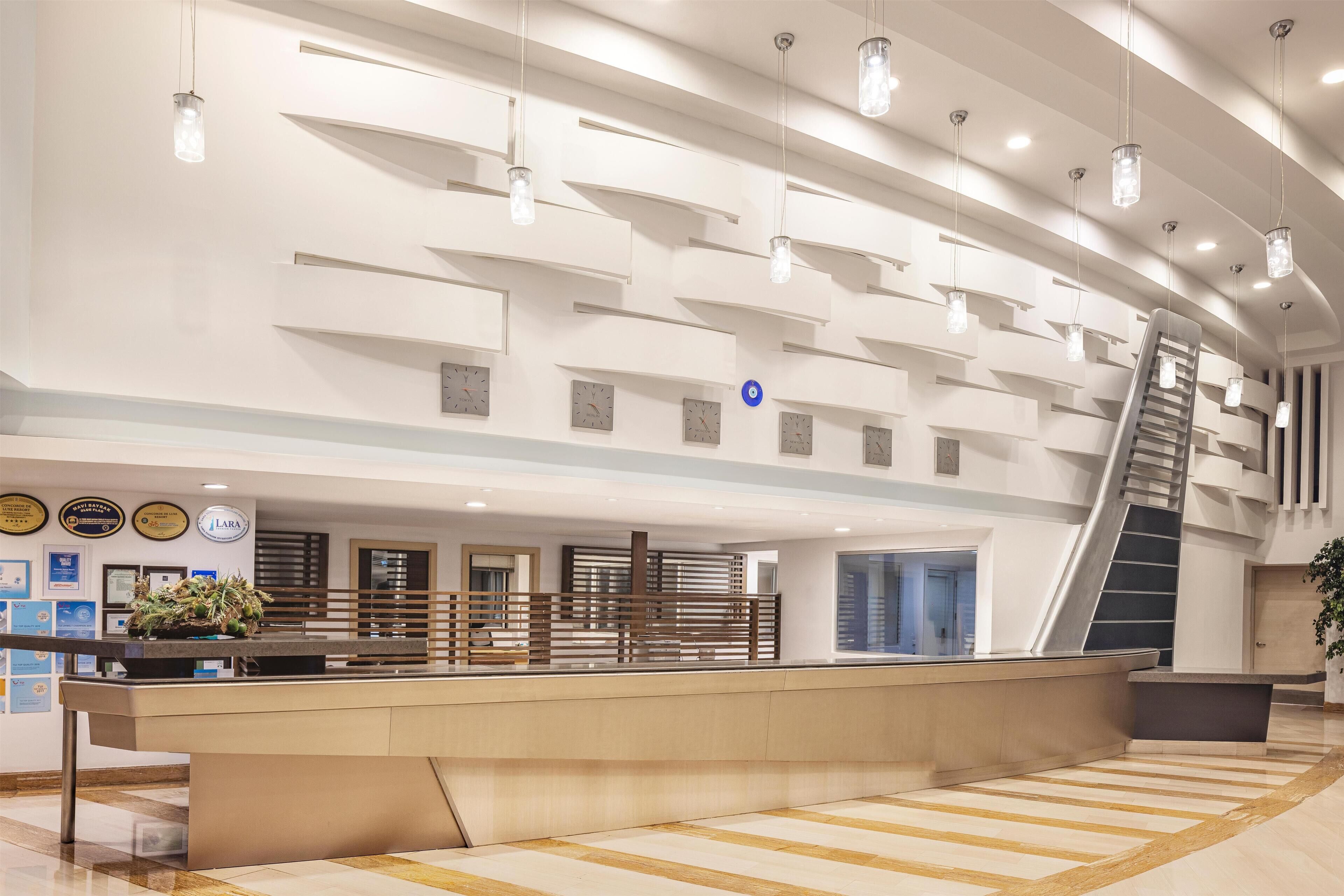 A modern hotel lobby with a reception desk, a staircase, and a large plant.