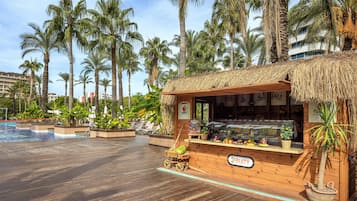 Quiosco de madera con techo de paja, un letrero que dice "FRUITY" y una exhibición de frutas y verduras.