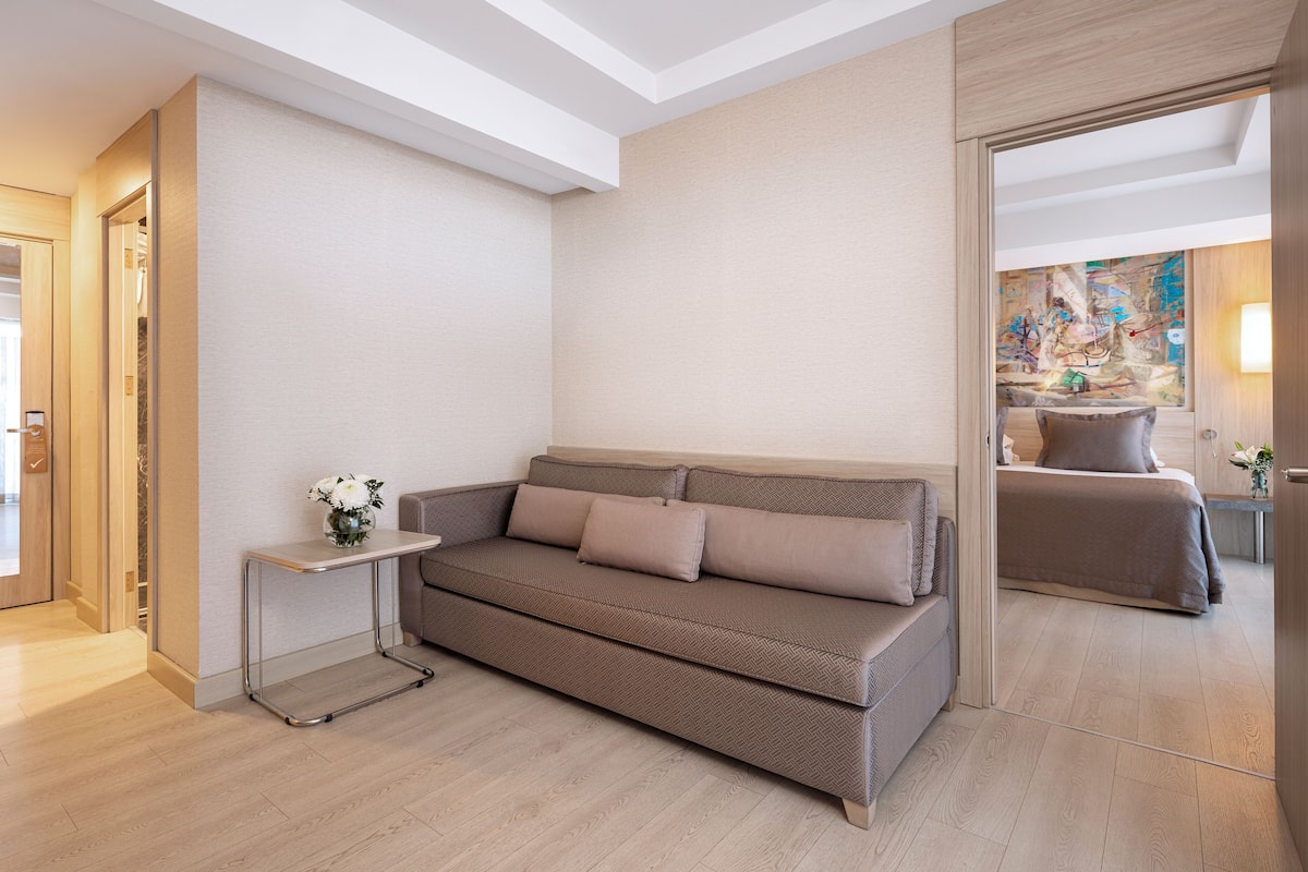 A modern hotel room with a sofa, a small side table, and a mirror.