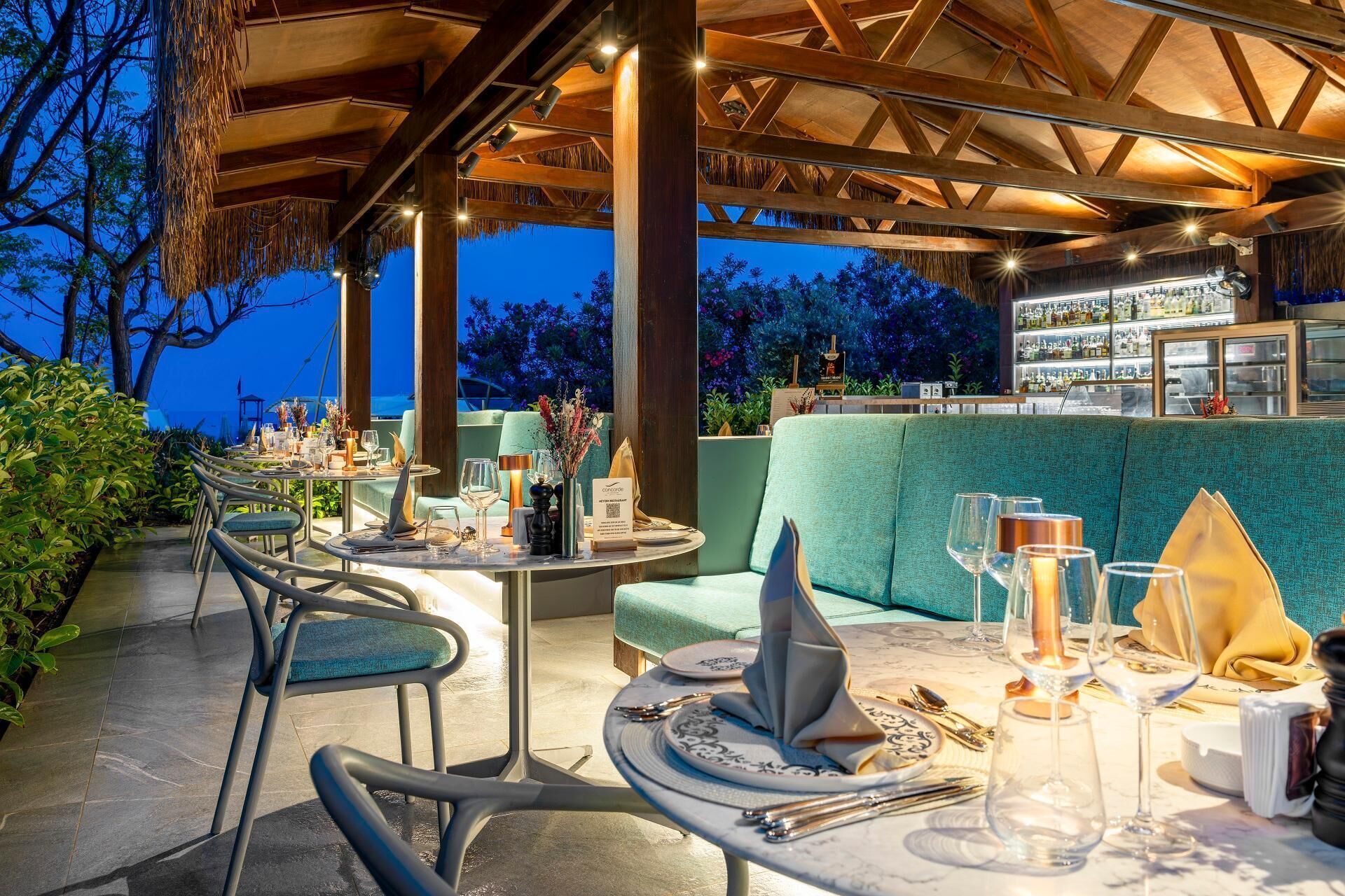 Un área de comedor al aire libre con mesas redondas, sillas y una barra de fondo.