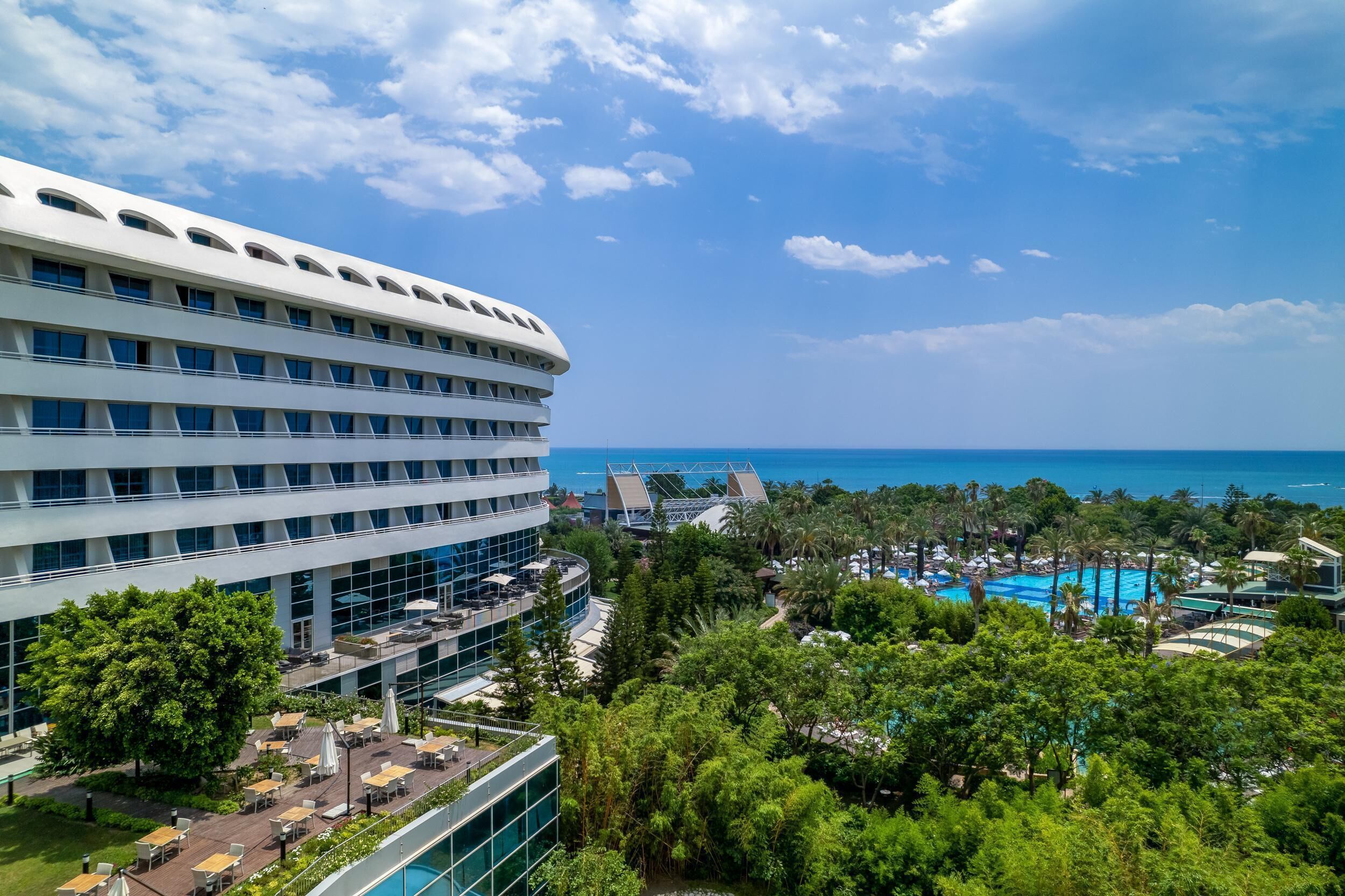 Un hotel moderno con piscina en la azotea, abundante vegetación y vista al océano.