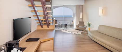 Habitación de hotel moderna con escalera de madera, televisor de pantalla plana, sofá y balcón con vista al mar.