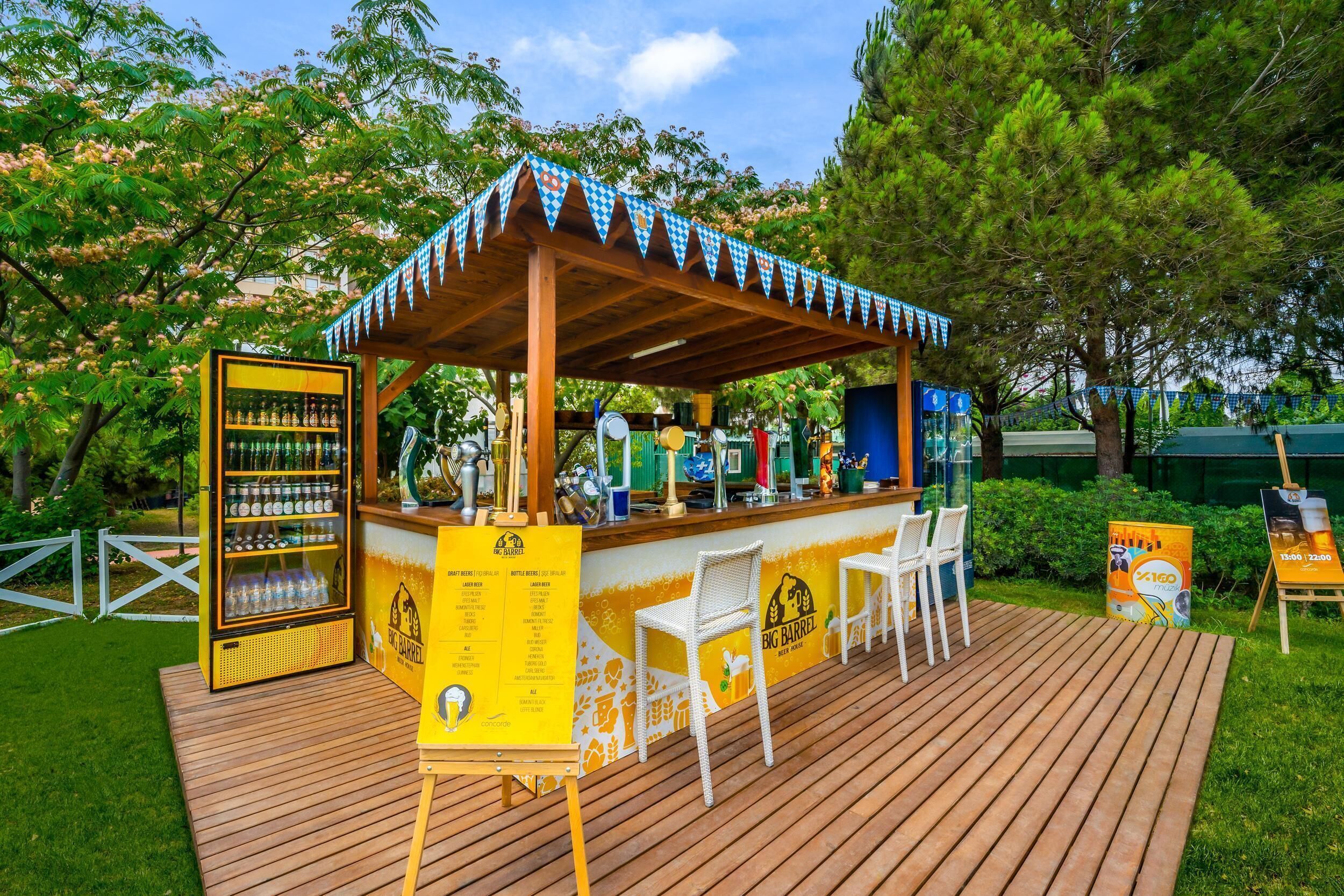 An outdoor bar area with a wooden deck, a beverage refrigerator, and a menu board.