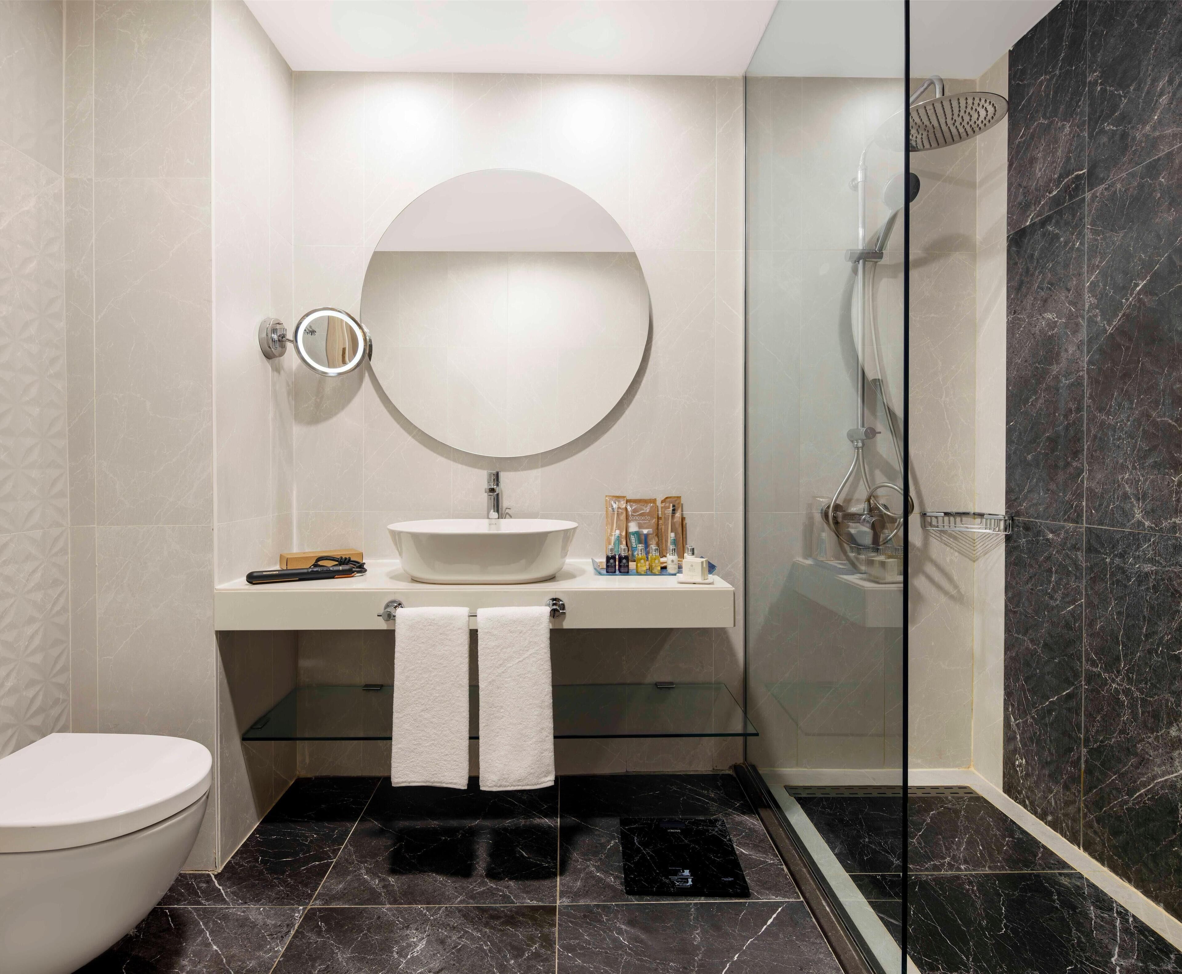 Une salle de bain moderne avec un grand miroir rond, un lavabo et une douche.