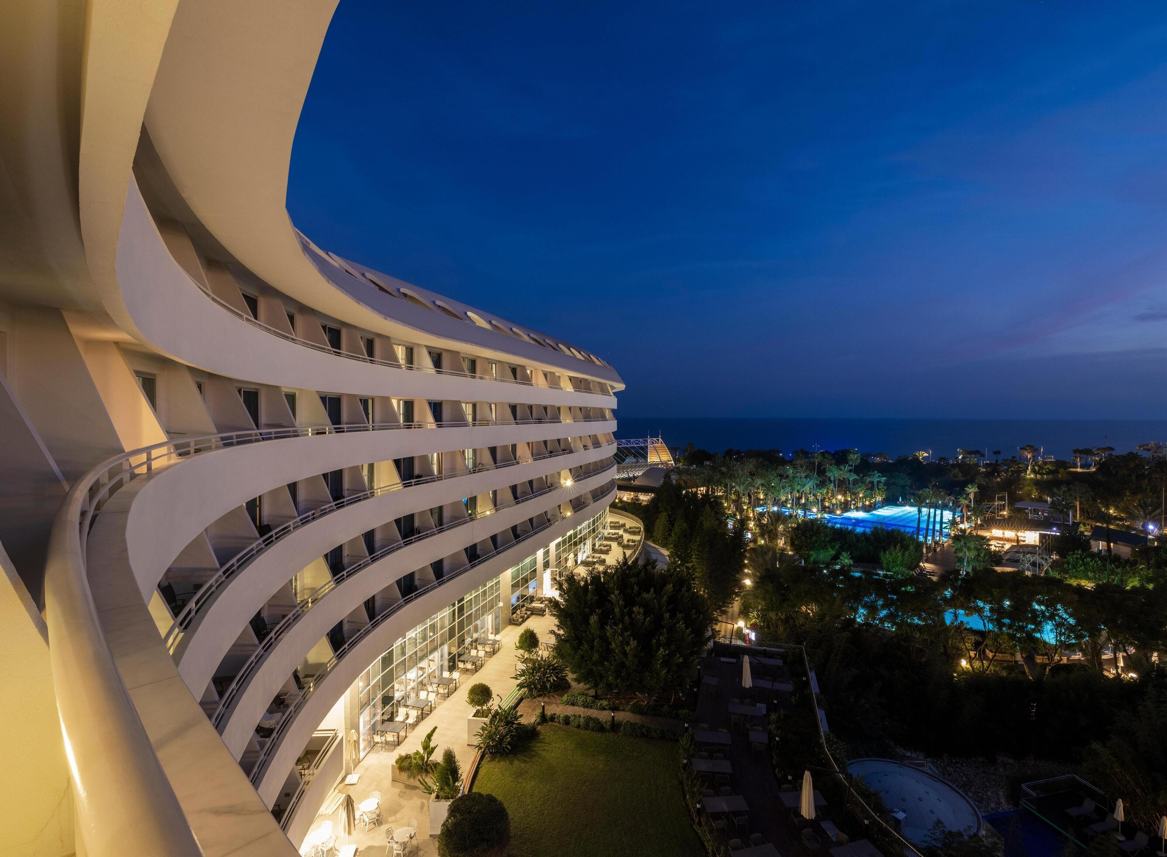 A modern hotel with multiple balconies, a pool area, and a view of the sea.