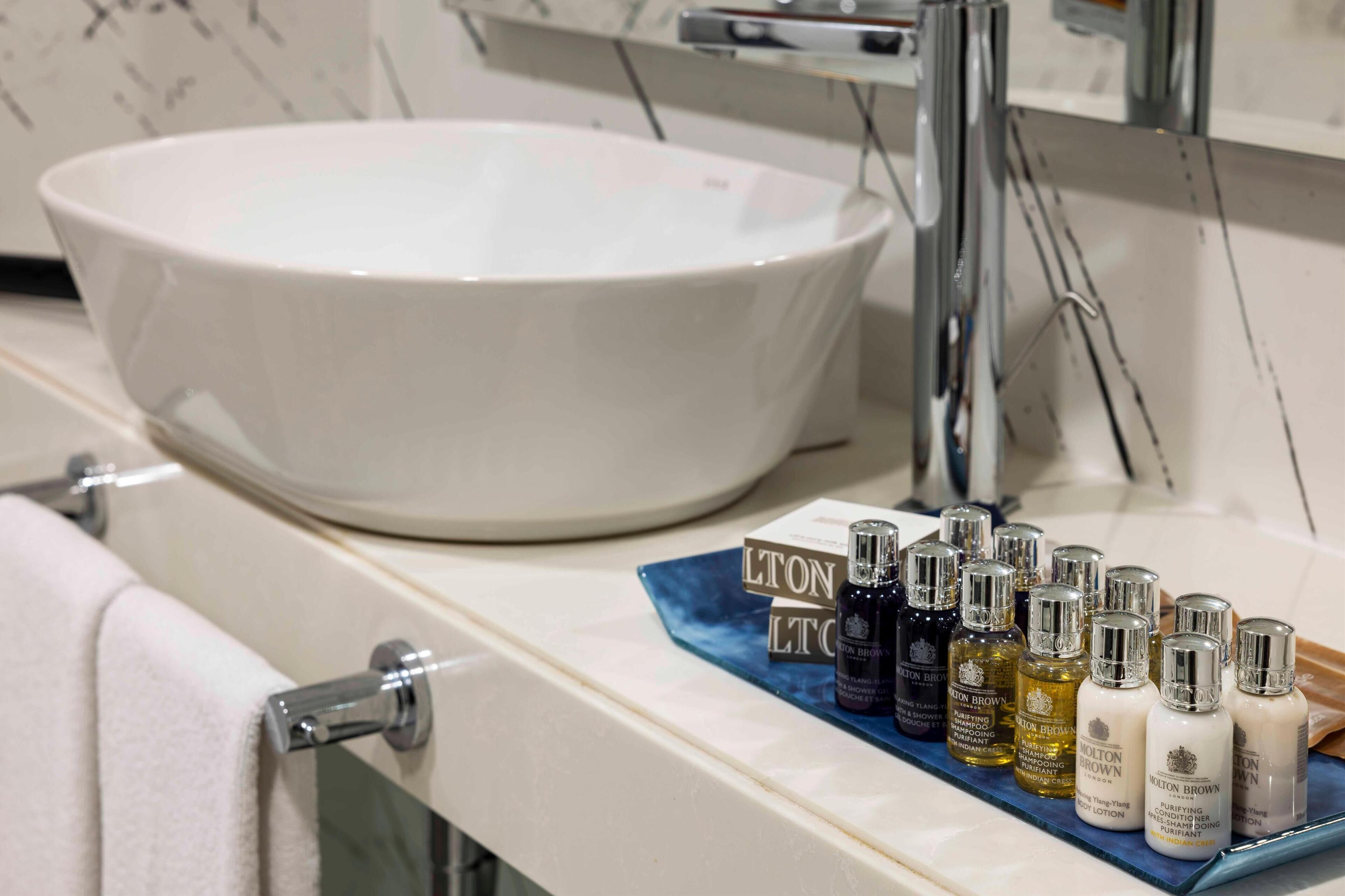 A bathroom with a large white basin, a towel rack, and a shelf with various toiletries.