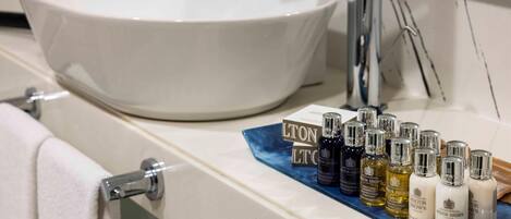 A bathroom with a large white basin, a towel rack, and a shelf with various toiletries.