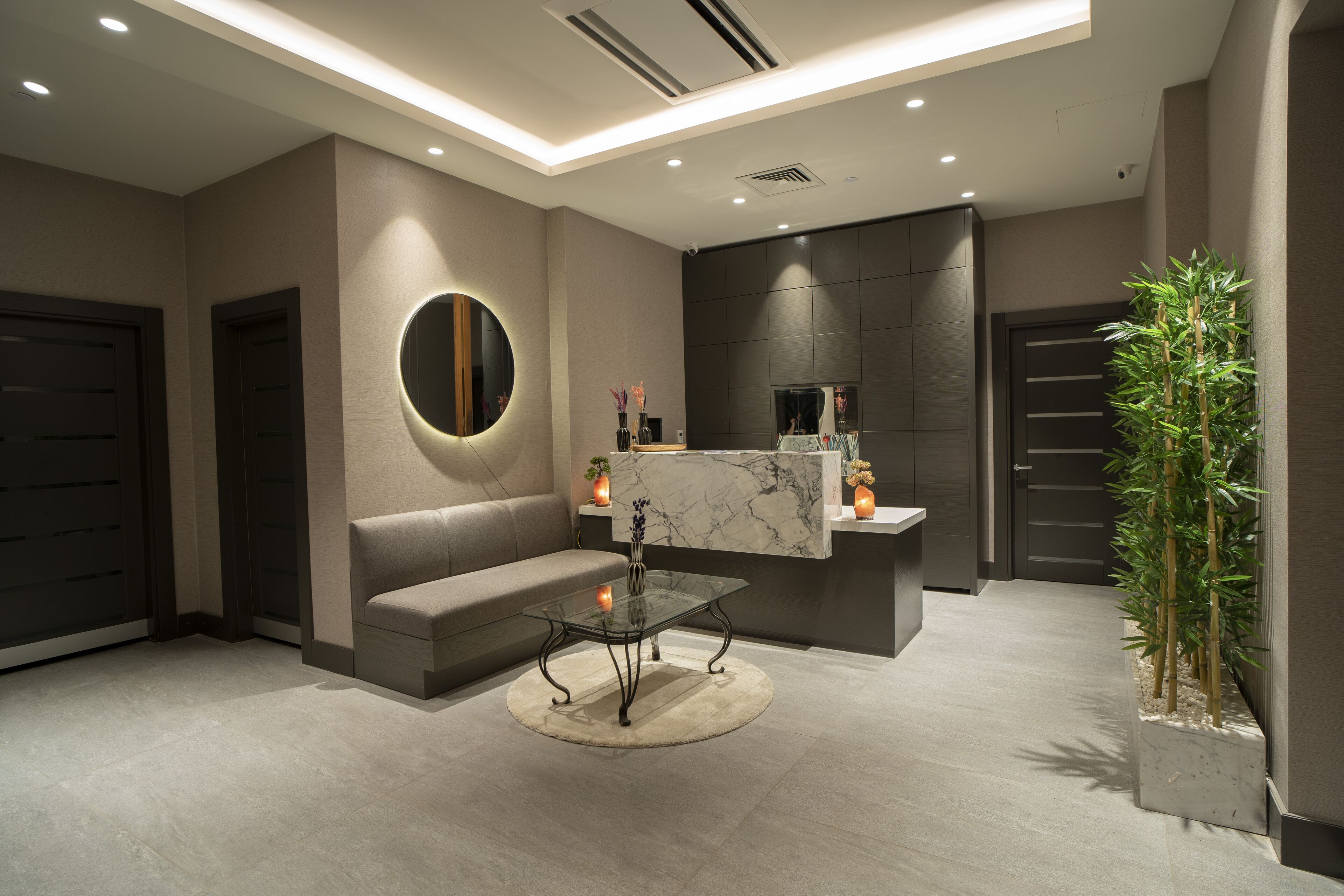 A modern interior with a glass coffee table, a round mirror, a sofa, and a reception desk.