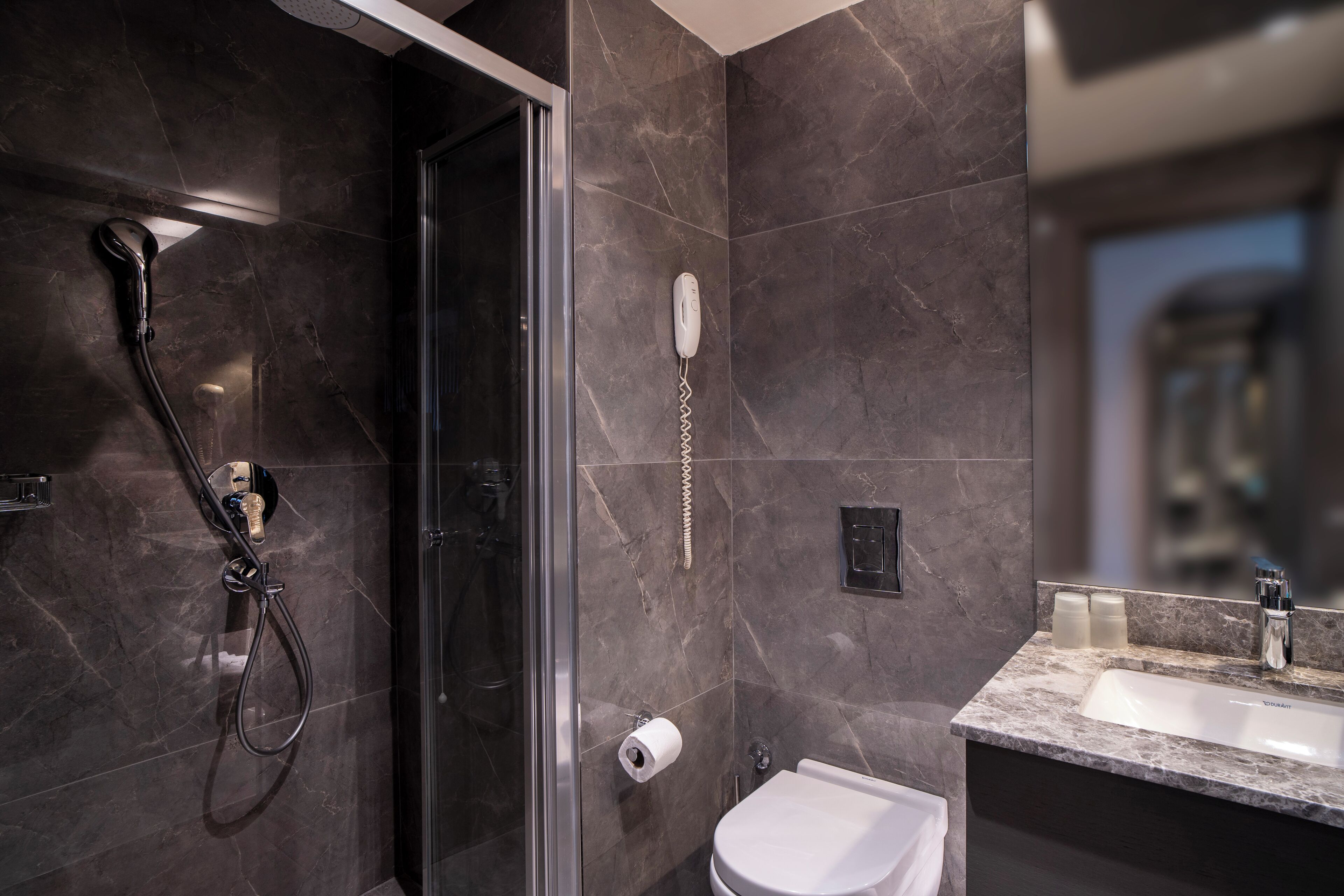 Un baño moderno con ducha envuelta en vidrio, inodoro y lavamanos con encimera de mármol.