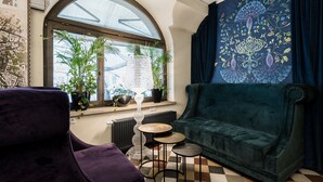 A cozy living room with a large window, a green sofa, a purple armchair, and a decorative tapestry.
