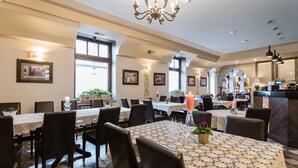 A spacious dining area with multiple tables, black chairs, and a chandelier.