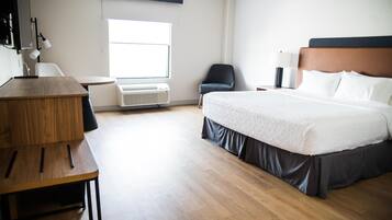 A hotel room with a bed, a desk, a chair, an air conditioning unit, and a window.