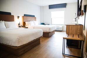 Et hotelværelse med to senge, et skrivebord, en stol, et natbord og et vindue med persienner.