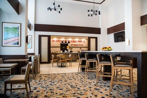 Un hall de hotel con zona de comedor, un ventanal con vistas y un cartel que indica servicio de desayuno.