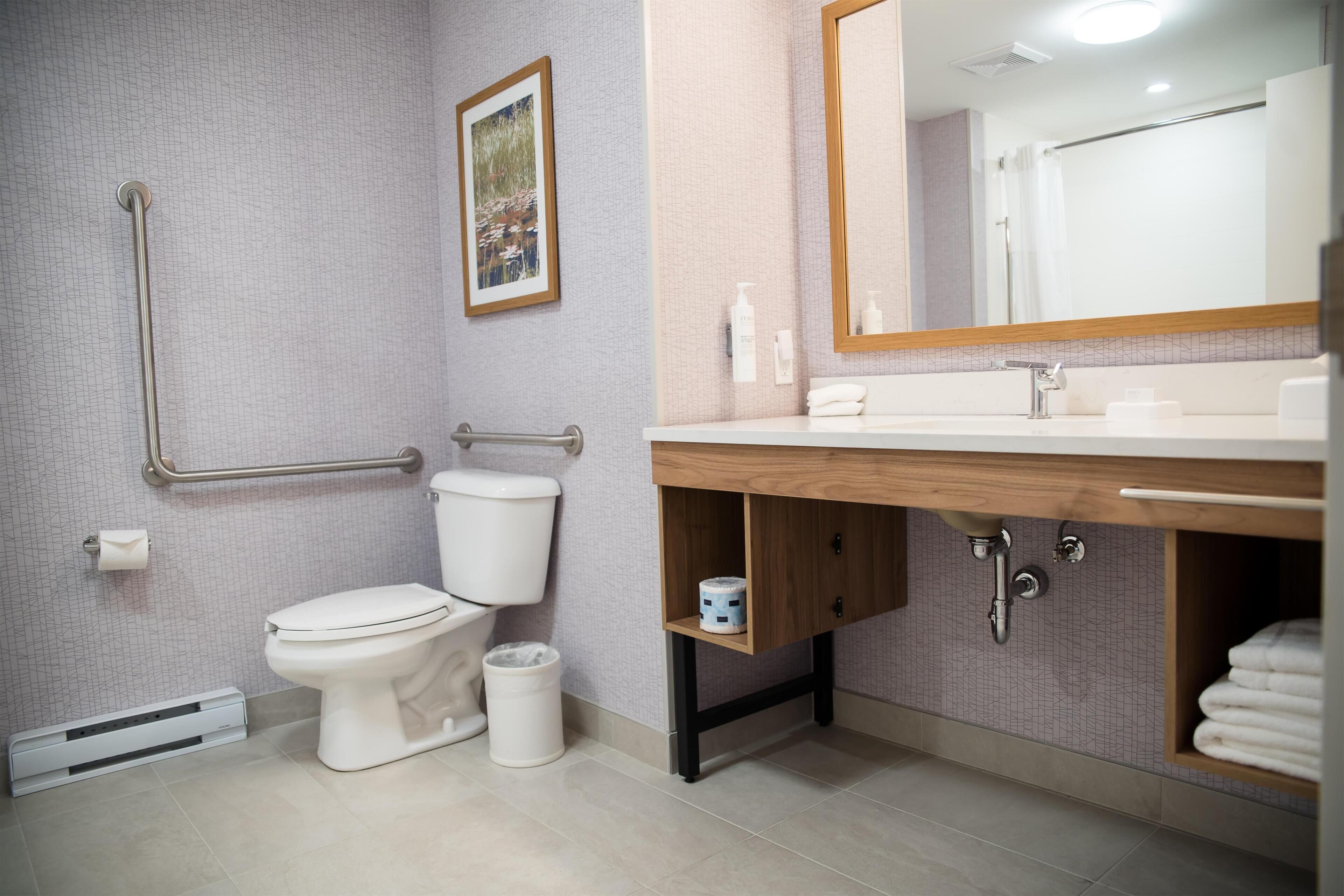 Une salle de bain moderne équipée d’un WC, d’un bidet, d’une barre d’appui, d’un lavabo, d’un miroir et d’un porte-serviettes.