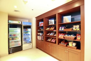 A vending area with snacks and beverages, including a refrigerator and shelves stocked with chips and drinks. - Hampton Inn & Suites by Hilton Laval (Laval)