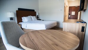 Et hotelværelse med seng, sengebord, stol og rundt bord.