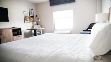 Habitación de hotel con cama, escritorio, silla, ventana y televisor de pantalla plana montado en la pared.