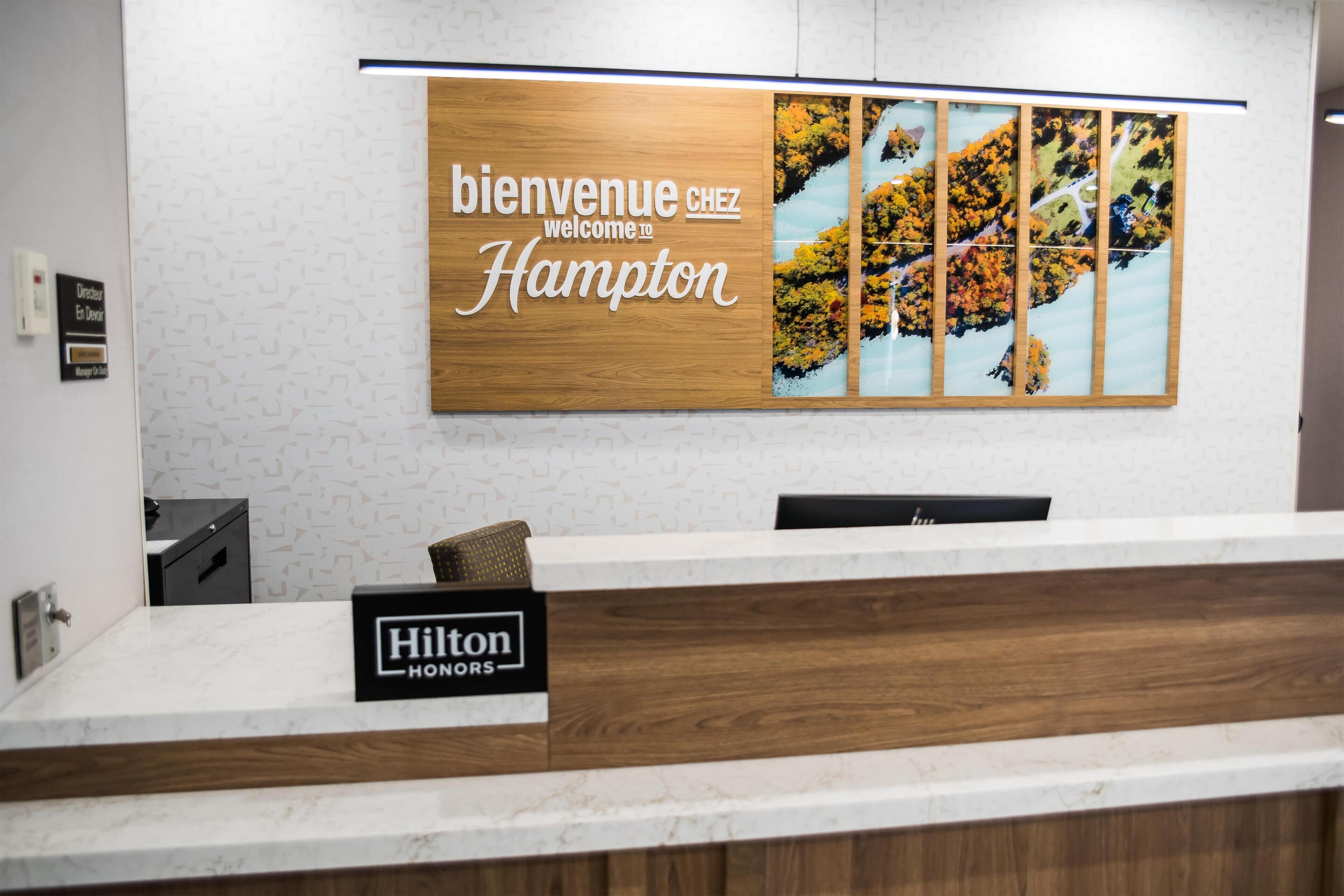 Una mesa de recepción con un cartel que dice 'Bienvenue chez Hampton' y un cartel de 'Hilton HONORS'.