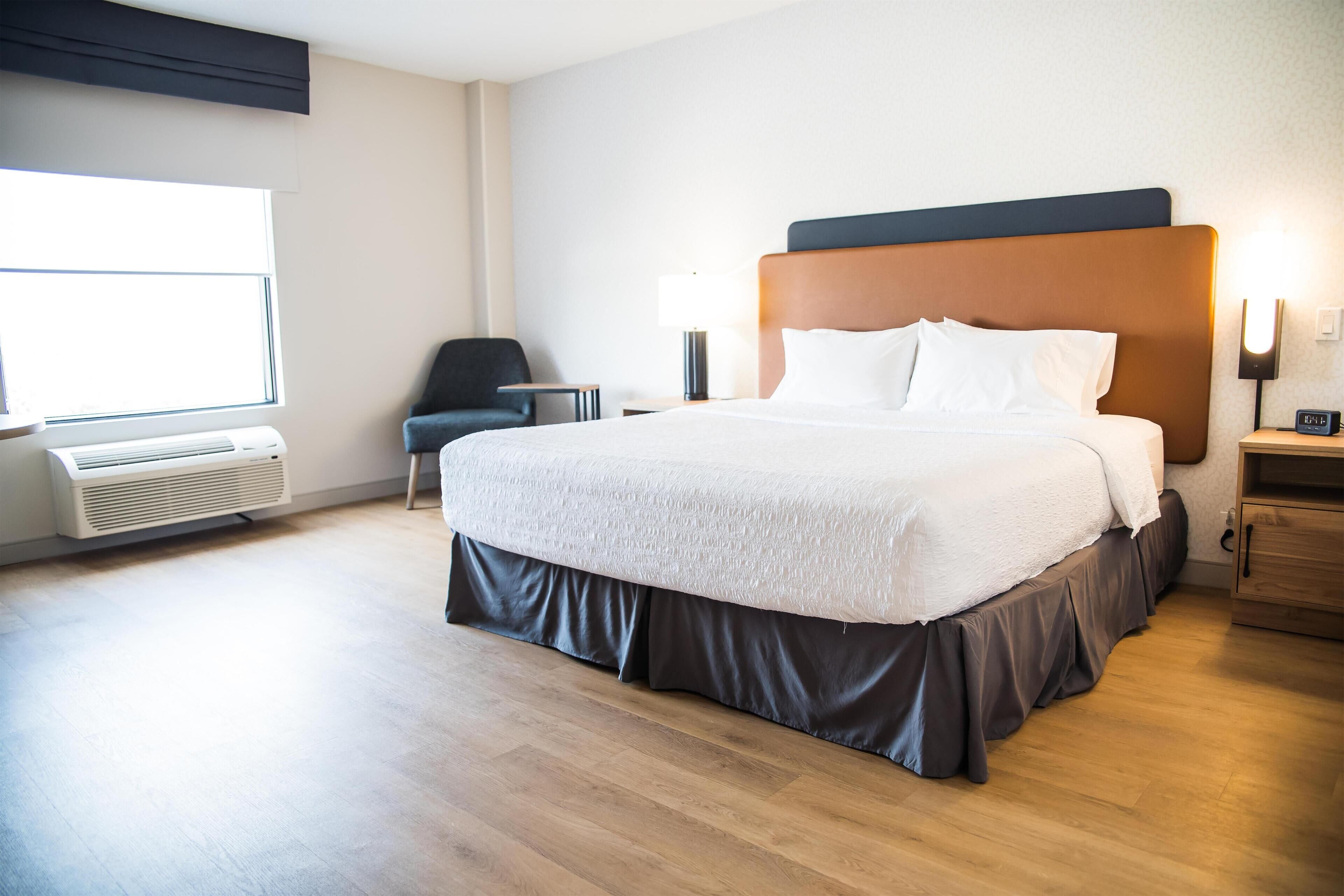 Ein Hotelzimmer mit einem großen Bett, einem Sessel, einem Nachttisch, einer Lampe und einem Wandheizkörper.
