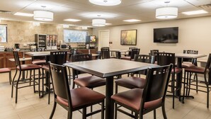 A spacious dining area with multiple tables and chairs, a kitchen area with appliances, and a television mounted on the wall. - Best Western Plus Sebastian Hotel & Suites (Sebastian)