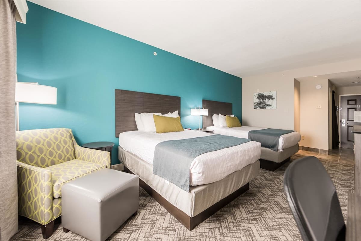 A hotel room with two beds, a sofa, a desk, and a chair.