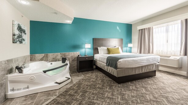 A modern hotel room with a large bed, a separate bathroom with a jacuzzi, and a view of the outdoors. - Best Western Plus Sebastian Hotel & Suites (Sebastian)